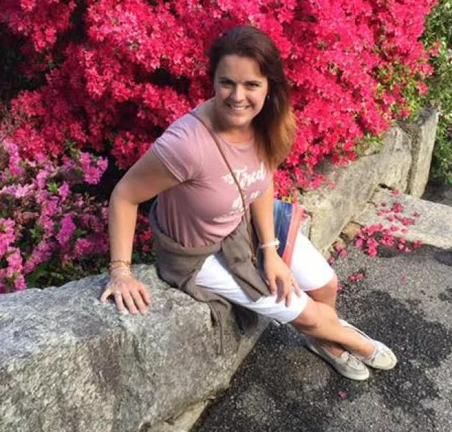 Woman sitting on a stone wall next to bright pink flowering bushes.