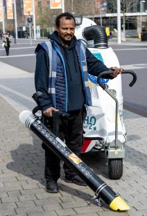 A street cleaner in Wembley, London, stands with a large leaf blower and a street cleaning machine.