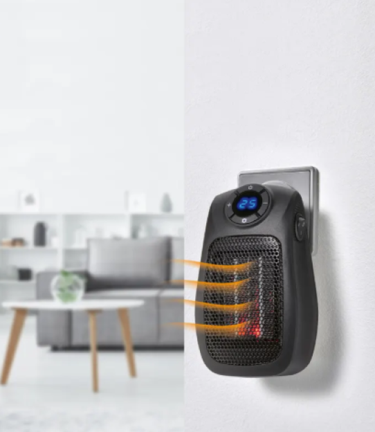A small black fan heater plugged into a wall outlet, blowing warm air into a blurred room.