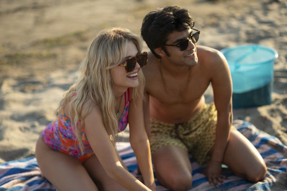 Emily Alyn Lind as Cadence Sinclair and Shubham Maheshwari as Gat sit on a striped towel on a sandy beach.