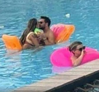 Couple kissing in a pool with another person in a pink floatie.
