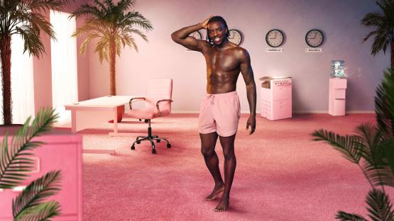 A shirtless man in pink shorts stands in a pink room with palm trees and office furniture.