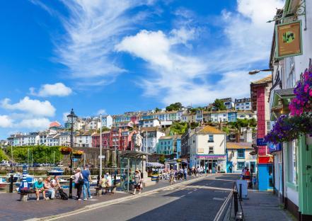 Brixham harbor, Devon, England, with colorful buildings and people.