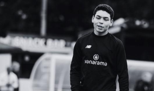 Black and white photo of a young man wearing a black sweatshirt with a logo.