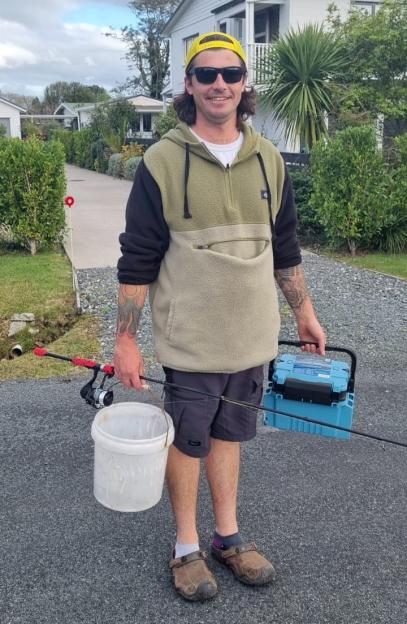 Man holding fishing rod, bucket, and tackle box.