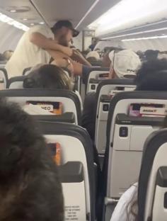 Video still of two passengers fighting on an airplane over a reclined seat.