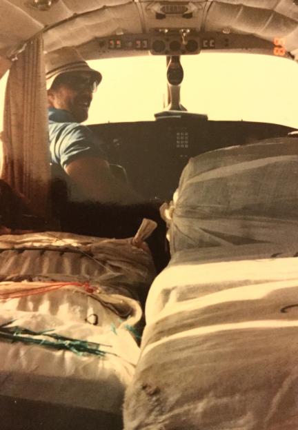 Man in a fedora hat piloting a small airplane packed with illicit cargo.