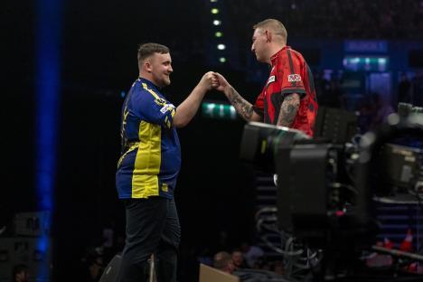 Luke Littler and Nathan Aspinall fist bumping at a darts tournament.
