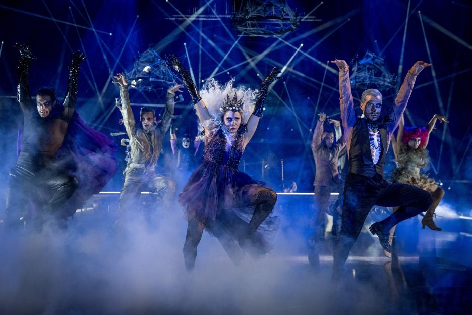 Dancers in Halloween costumes on a stage with blue lighting and fog.