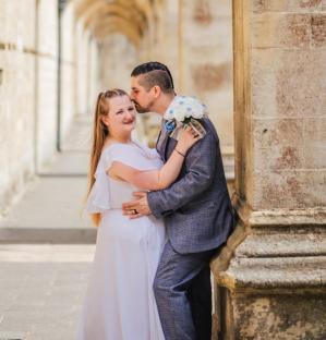 A bride and groom embrace near a stone column.