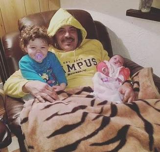 Man in a yellow hoodie holding two babies.
