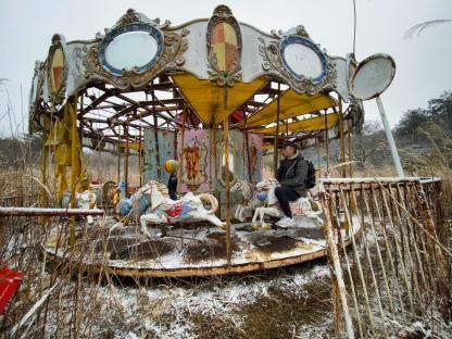 Person sitting on a carousel horse in an abandoned theme park.