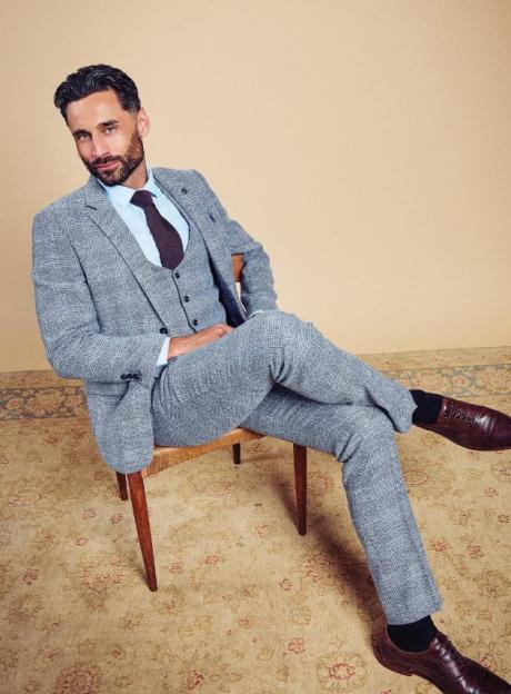 Luke Harden, a man with a beard, wearing a light blue shirt, brown tie, and a gray patterned three-piece suit, seated in a chair.