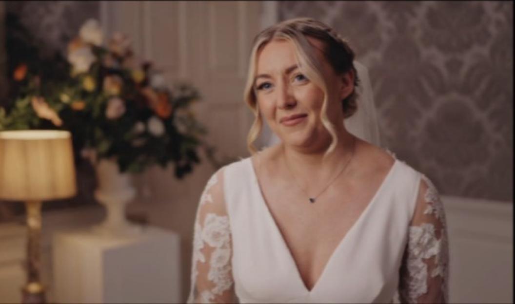 A blonde bride in a white dress with lace sleeves smiles.