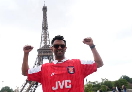 Arsenal fan in Ian Wright jersey celebrating in Paris with Eiffel Tower in background.