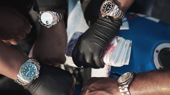 Close-up of hands wearing expensive watches and black gloves handling stacks of cash.