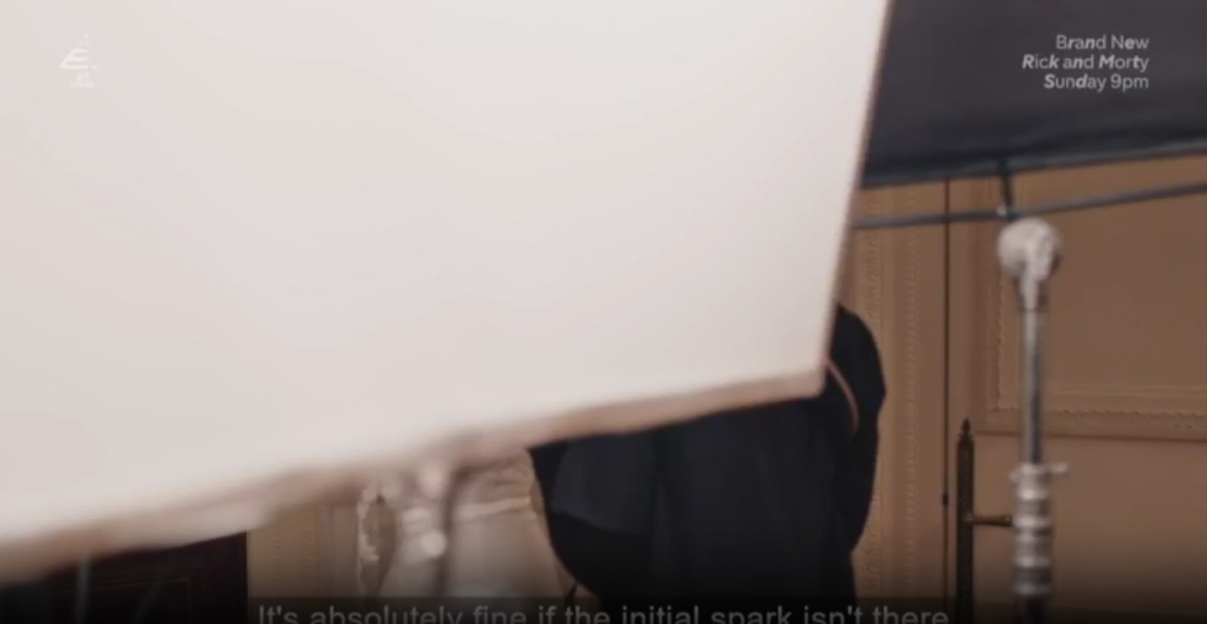 A television screen showing a partially obscured scene with a white object in the foreground, a person in dark clothing, and a light stand, with "Brand New Rick and Morty Sunday 9pm" and "It's absolutely fine if the initial spark isn't there" text overlays.