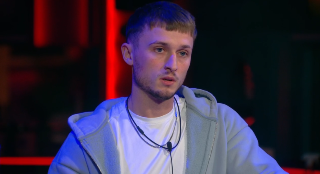 A young man with light brown hair and a short fringe, wearing a white t-shirt and a light gray zip-up hoodie, with two necklaces around his neck.