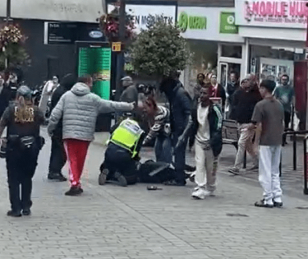 Police officer apprehending a man with another man pointing at him.