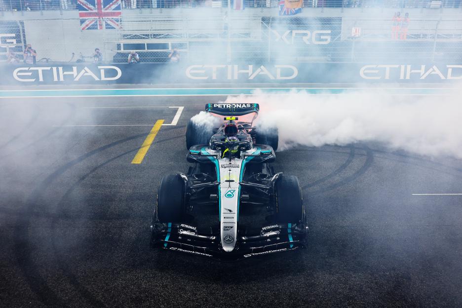 Lewis Hamilton performing donuts in his Mercedes W15 on the track, surrounded by smoke, during the Abu Dhabi Grand Prix.