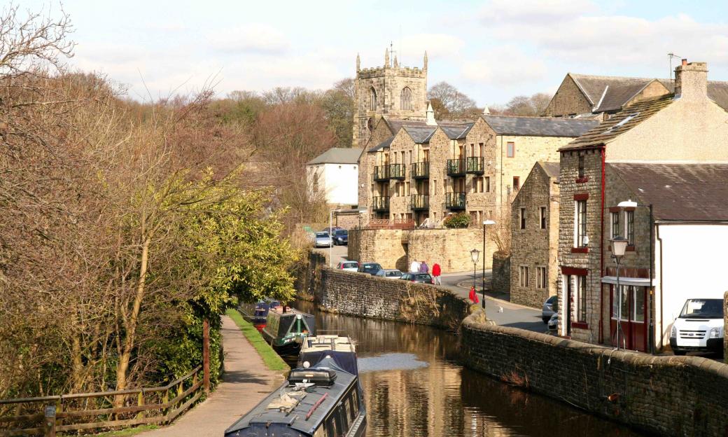 A canal with boats on the left, a stone wall along the right bank leading to buildings and a church in the background.