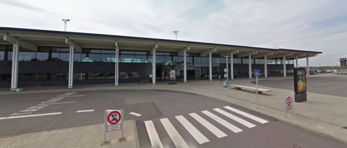Exterior of a modern airport terminal building with a wide road in front and a crosswalk.