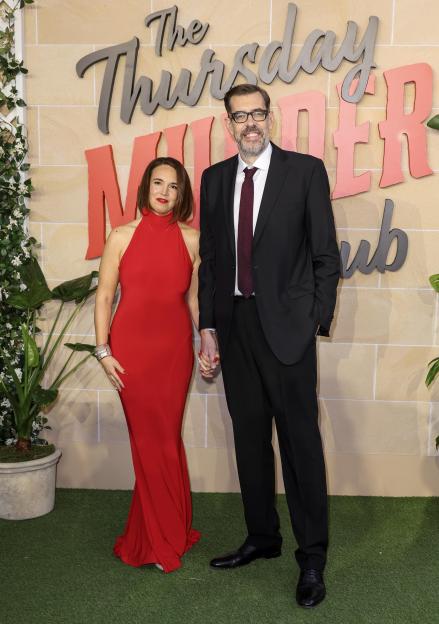 Ingrid Oliver in a red dress and Richard Osman in a suit holding hands at 'The Thursday Murder Club' UK Premiere.