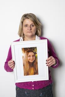 Woman holding framed photo of her deceased daughter.