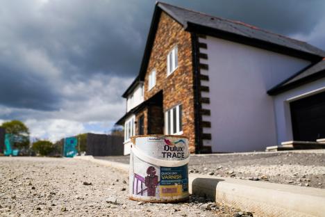 A paint can sits on the ground in front of a new, unfinished house.