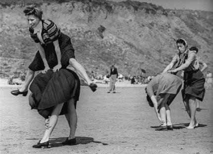 Holidaymakers playing leapfrog on a beach.