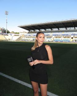 Woman in black dress holding microphone at soccer stadium.