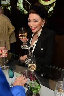 Joan Collins at a book launch, holding a glass of wine.