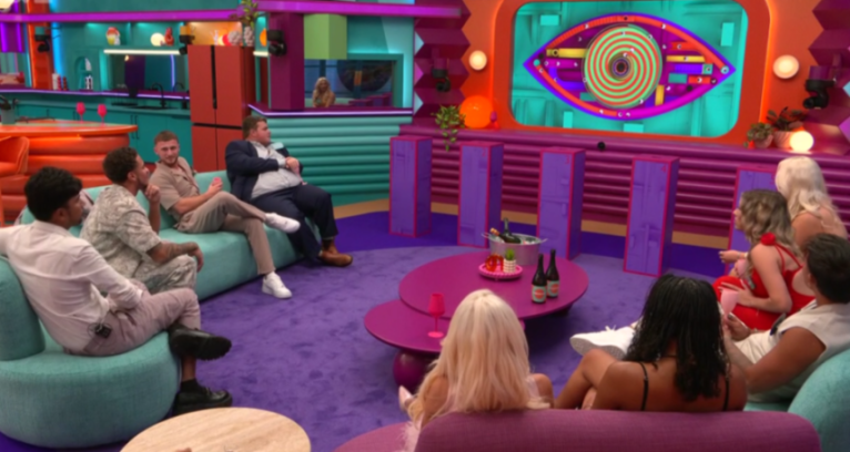 Contestants watch a Big Brother Eye screen in the living room.