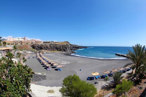 Black sand beach with blue umbrellas and lounge chairs in Tenerife, Spain.