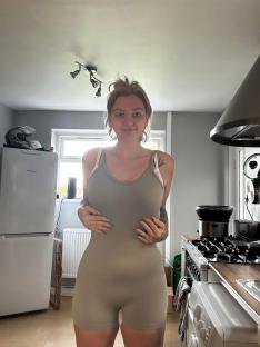 Woman in a taupe bodysuit in her kitchen.