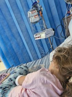 A young girl in a hospital bed connected to medical equipment.