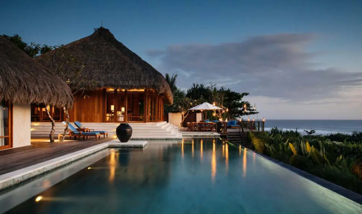 Oceanfront villa with infinity pool and thatched roof.