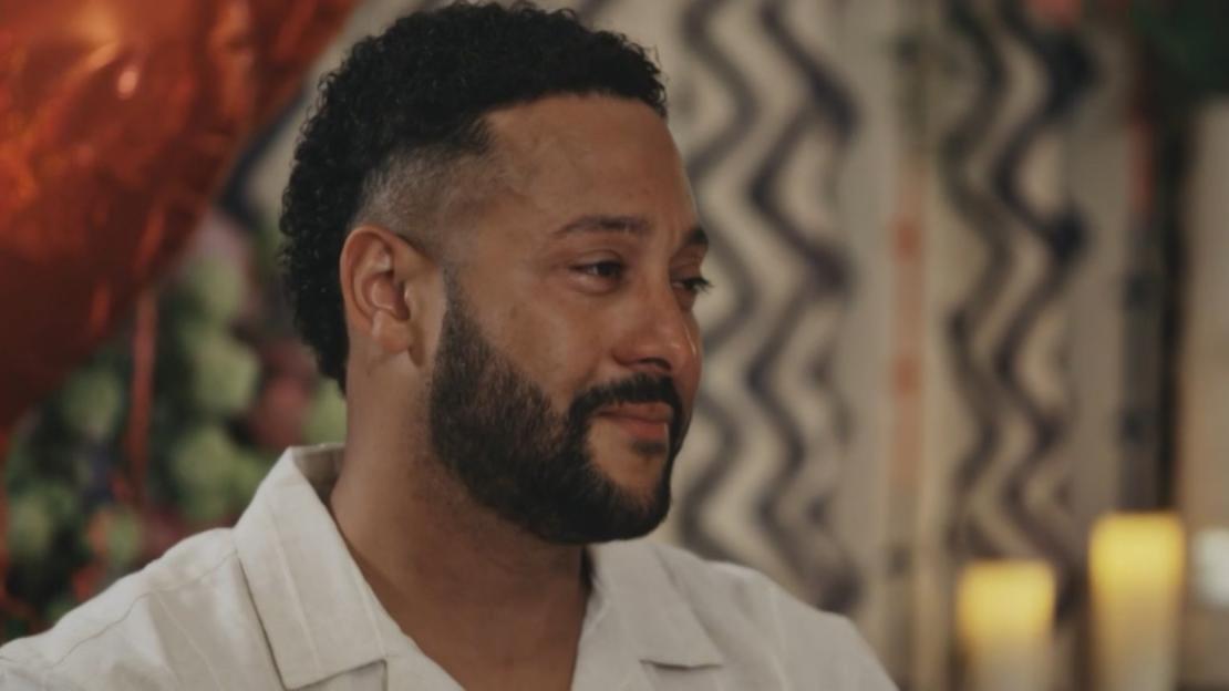 A man with a beard, wearing a light-colored collared shirt, with tears in his eyes.