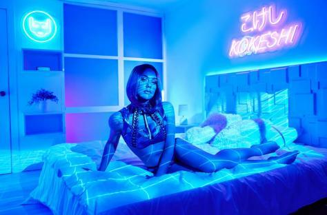 Illustration of a female robot sitting on a bed in a futuristic city.