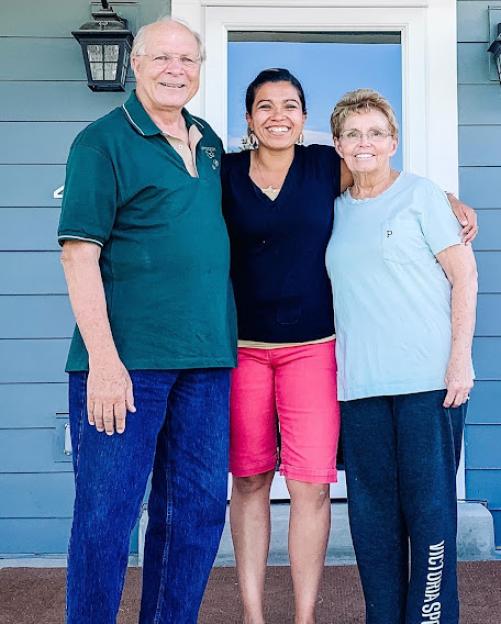 A woman with her adoptive parents smiling in front of a house.