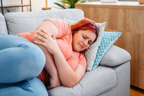 A young plus-size woman lying on a sofa, experiencing period cramps.