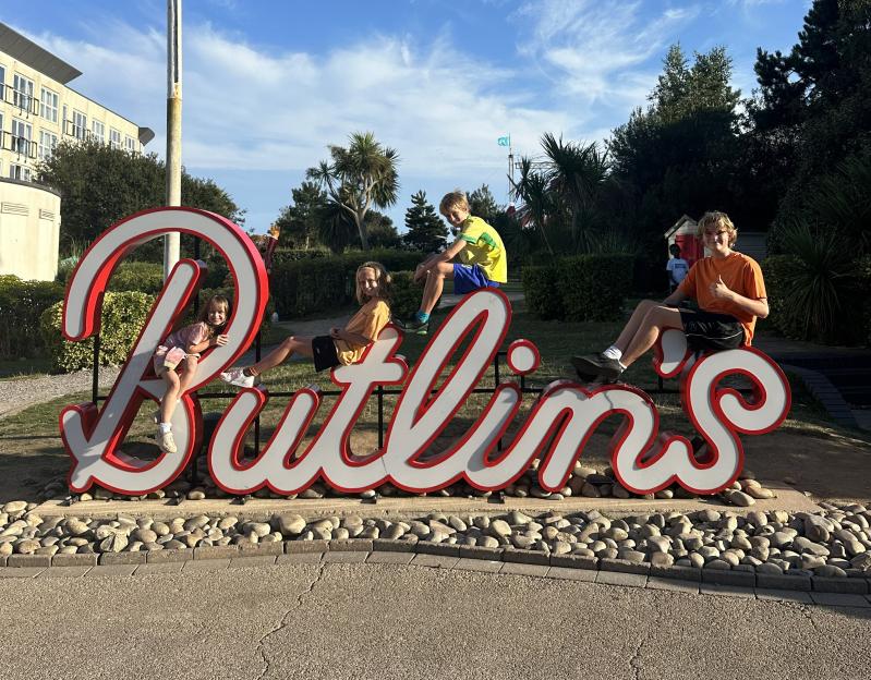 Four children sitting on a Butlin's sign.