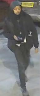 Surveillance image of a person wearing dark clothing and a hood.