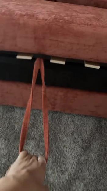 A person pulling an orange fabric strap to open a sofa bed.