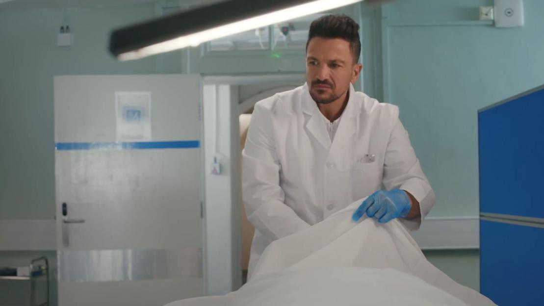 Peter Andre, portraying a pathologist, prepares a body for examination.