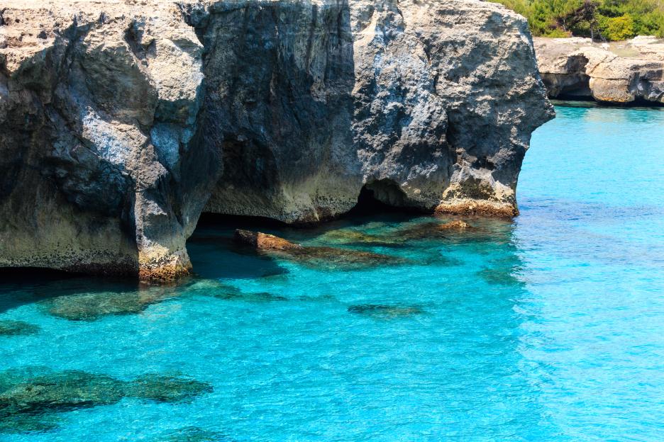 Adriatic Sea coast at Roca Vecchia, Salento, Puglia, Italy, featuring clear turquoise water and large rock formations with small caves at the water's edge.