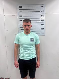 Mugshot of a man in a mint green shirt and black shorts.
