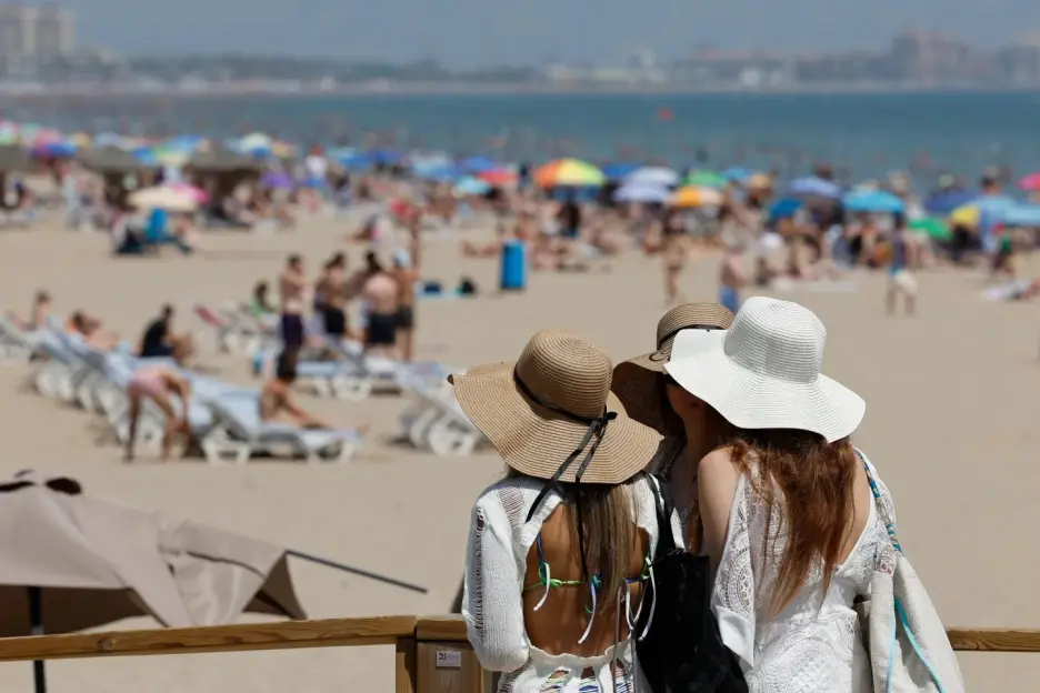 Two women wearing sun hats on a crowded beach.