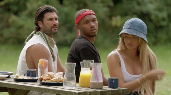Three people sitting at a picnic table outdoors, looking tense.