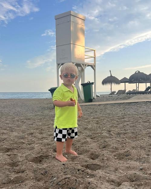 Oliver Pugh, a young boy with blonde hair and sunglasses, standing on a beach in Marbella, Spain.